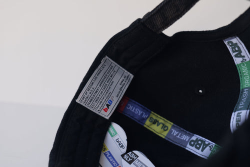 Interior view of the bABP B-SIDE black washed cotton hat showing the "Port of Design: Los Angeles" heritage label, branded recycling-themed seam tapes, and internal logo embroidery