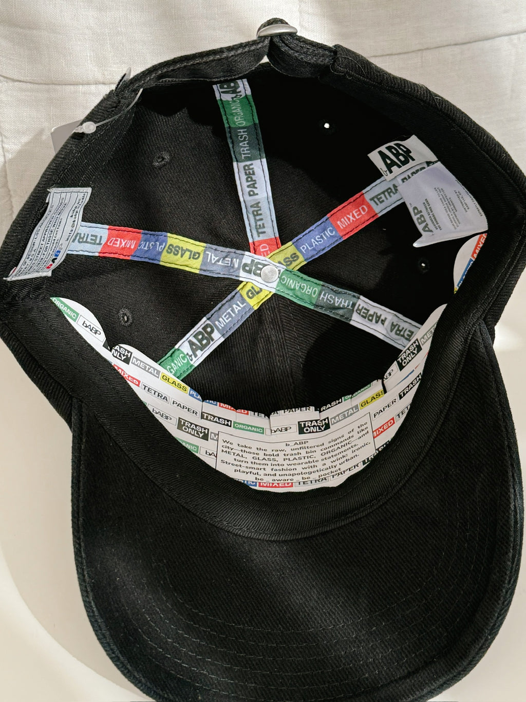 Interior view of bABP "COMPOST" black washed cotton hat from the B-SIDE collection, showing branded interior taping, logo patches with hidden details, signature tags, and custom branded cardboard insert
